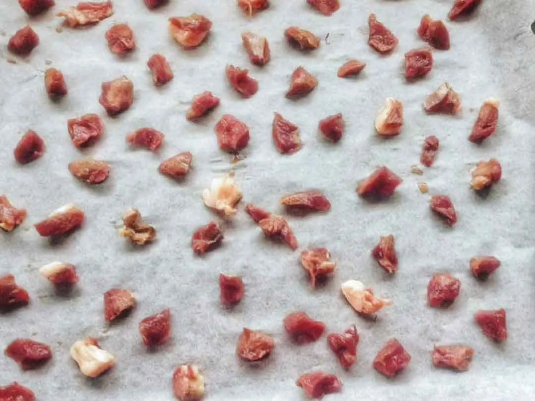 Pezzetti di cuore crudo disposti su carta da forno, pronti per l'essiccazione
